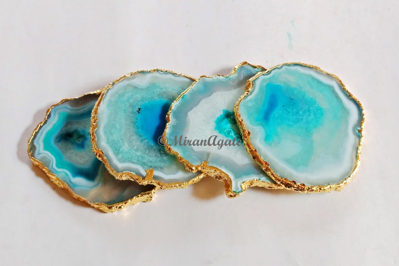 May include: Four agate coasters with gold trim. The coasters are a light blue and white color with a swirling pattern.