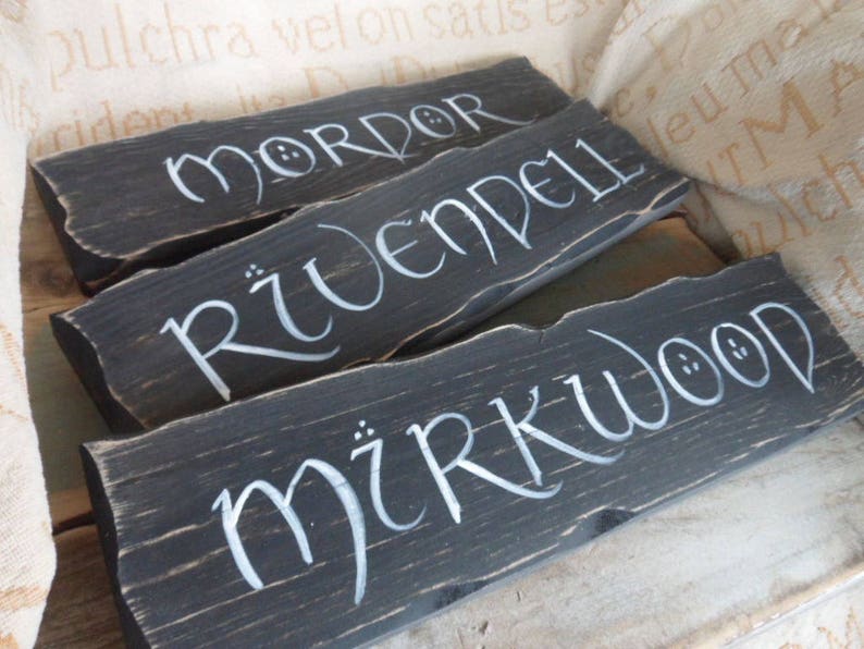 Pu&ograve; includere: Tre cartelli di legno dipinti di nero con lettere bianche. I cartelli recitano "Mordor", "Rivendell" e "Mirkwood".