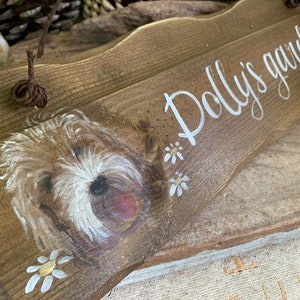 K&ouml;nnte beinhalten: Ein Holzschild mit einem gemalten Hund und dem Text "Polly's garden". Das Schild ist braun mit wei&szlig;en Farbakzenten und hat ein Seil zum Aufh&auml;ngen.