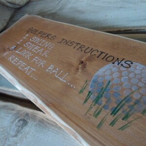 Puede incluir: Se&ntilde;al de madera con el texto "Golfers Instructions" y una lista de instrucciones: 1. Swing, 2. Swear, 3. Look for ball, 4. Repeat. Una bola de golf blanca con hierba verde est&aacute; pintada en la se&ntilde;al.