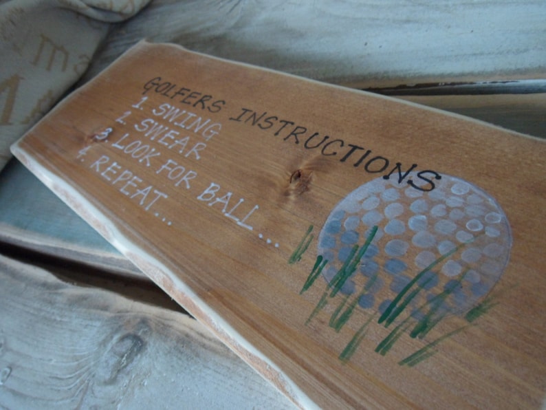 Puede incluir: Se&ntilde;al de madera con el texto "Golfers Instructions" y una lista de instrucciones: 1. Swing, 2. Swear, 3. Look for ball, 4. Repeat. Una bola de golf blanca con hierba verde est&aacute; pintada en la se&ntilde;al.