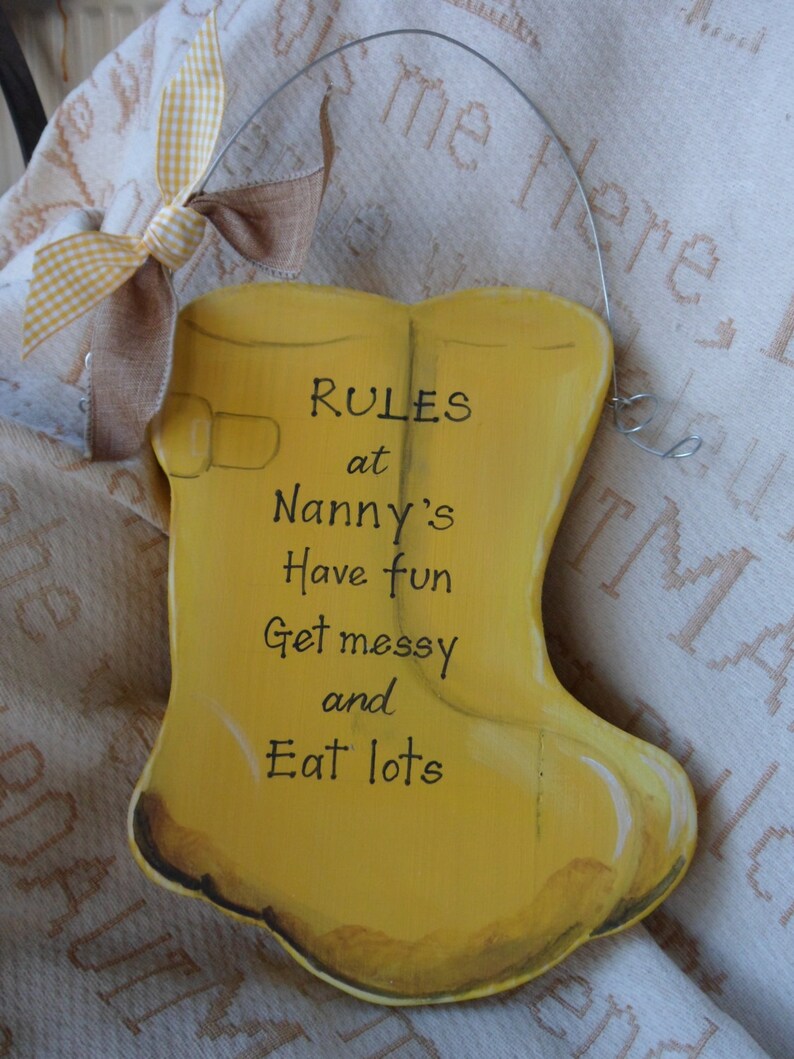 K&ouml;nnte beinhalten: Gelbes Holzschild in Form eines Gummistiefels mit dem Text "RULES at Nanny's Have fun Get messy and Eat lots" in Schwarz.