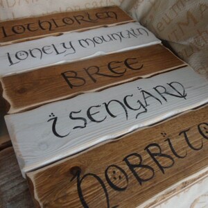 Pu&ograve; includere: Cinque cartelli in legno con vernice bianca e lettere nere. I cartelli recitano "Lothlorien", "Lonely Mountain", "Bree", "Isengard" e "Hobbiton".