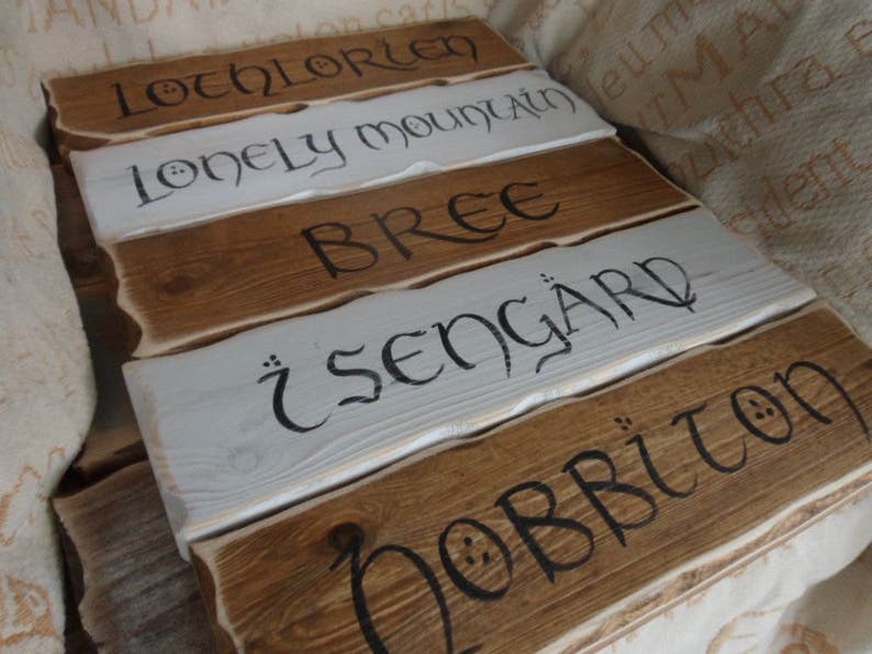 Pu&ograve; includere: Cinque cartelli in legno con vernice bianca e lettere nere. I cartelli recitano "Lothlorien", "Lonely Mountain", "Bree", "Isengard" e "Hobbiton".