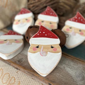 Può includere: Ornamenti in legno di Babbo Natale dipinti a mano, con cappelli rossi e barbe bianche. Gli ornamenti presentano guance e nasi rosa. Decorazione festiva per le festività natalizie.