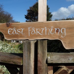May include: A wooden sign with the words "East Farthing" written in white paint. The sign is attached to a wooden post.