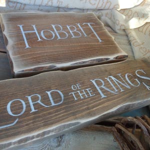 Pu&ograve; includere: Due cartelli in legno con le parole "Lo Hobbit" e "Il Signore degli Anelli" scritte in vernice bianca.