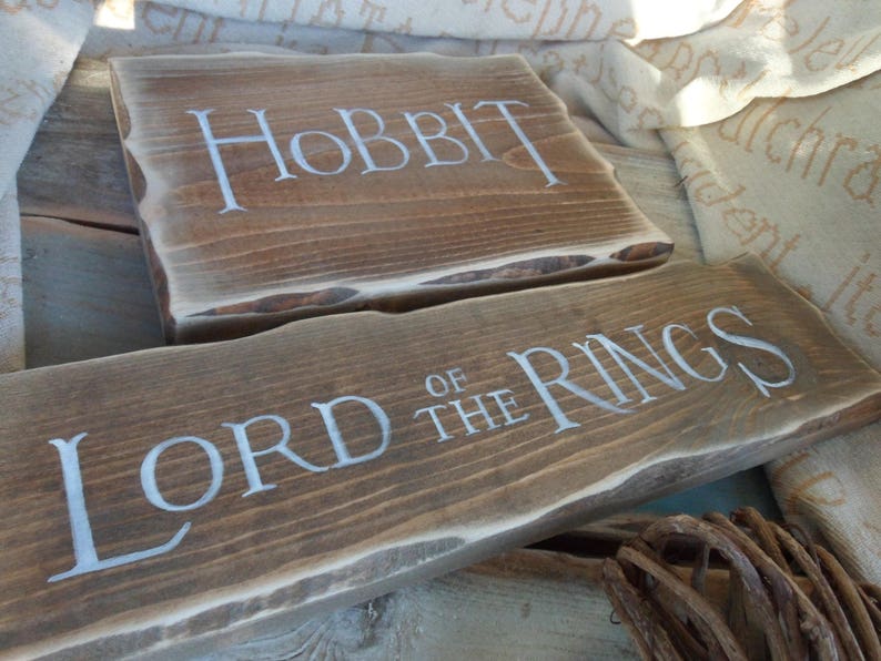 Pu&ograve; includere: Due cartelli in legno con le parole "Lo Hobbit" e "Il Signore degli Anelli" scritte in vernice bianca.