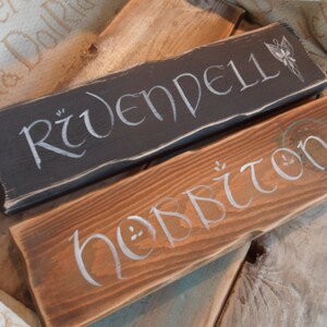 Pu&ograve; includere: Due cartelli in legno con lettere bianche. Il cartello superiore &egrave; nero e dice "Rivendell". Il cartello inferiore &egrave; marrone e dice "Hobbiton".