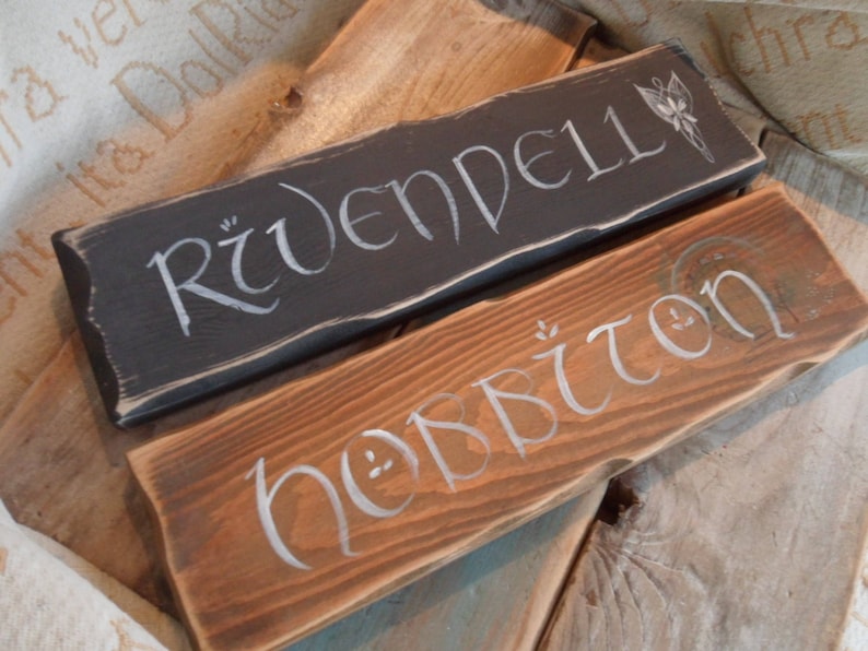 Pu&ograve; includere: Due cartelli in legno con lettere bianche. Il cartello superiore &egrave; nero e dice "Rivendell". Il cartello inferiore &egrave; marrone e dice "Hobbiton".