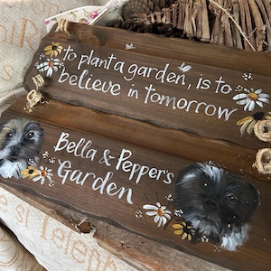 K&ouml;nnte beinhalten: Zwei Holzschildchen mit gemalten Blumen und dem Text "Einen Garten zu pflanzen, bedeutet, an morgen zu glauben" und "Bella & Peppers Garten".