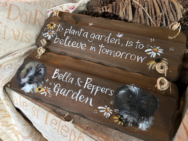 K&ouml;nnte beinhalten: Zwei Holzschildchen mit gemalten Blumen und dem Text "Einen Garten zu pflanzen, bedeutet, an morgen zu glauben" und "Bella & Peppers Garten".