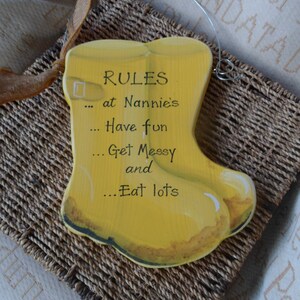 K&ouml;nnte beinhalten: Gelbes Holzschild in Form eines Gummistiefels mit dem Text "RULES at Nannie's... Have fun... Get Messy and... Eat lots"