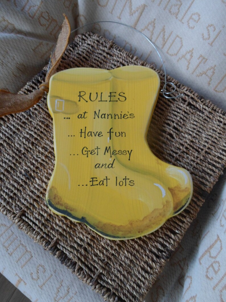 K&ouml;nnte beinhalten: Gelbes Holzschild in Form eines Gummistiefels mit dem Text "RULES at Nannie's... Have fun... Get Messy and... Eat lots"