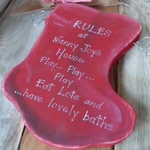 K&ouml;nnte beinhalten: Roter Holzstrumpf mit wei&szlig;em Text, der "RULES at Nanny Joy's House Play... Play... Eat Lots and have lovely baths" lautet.