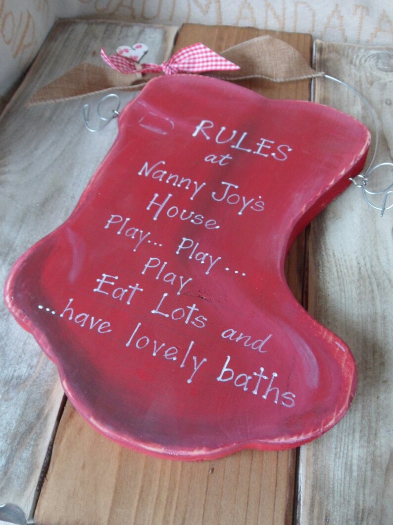 K&ouml;nnte beinhalten: Roter Holzstrumpf mit wei&szlig;em Text, der "RULES at Nanny Joy's House Play... Play... Eat Lots and have lovely baths" lautet.