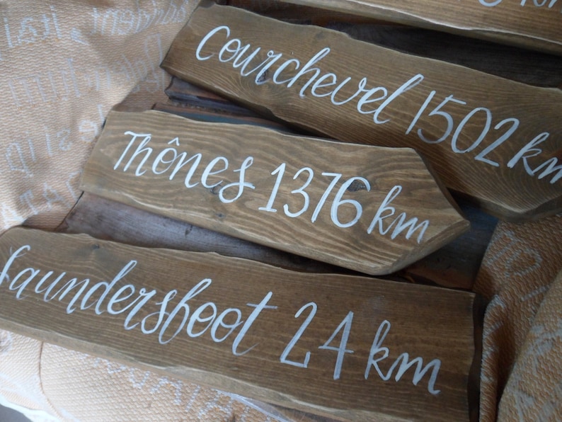 Pu&ograve; includere: Segnali stradali in legno con scritte bianche. I segnali indicano le distanze in chilometri verso varie localit&agrave;: Courchevel 1502 km, Th&ocirc;nes 1376 km e Laundersfoot 24 km. Il legno ha una finitura marrone naturale.