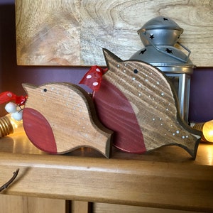 May include: Two wooden bird ornaments featuring natural wood grain, painted red chests, and white dotted details. Each bird is adorned with a small red ribbon with white polka dots and a tiny white berry accent near the head.