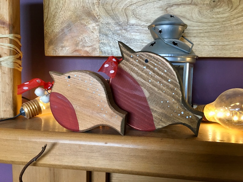 May include: Two wooden bird ornaments featuring natural wood grain, painted red chests, and white dotted details. Each bird is adorned with a small red ribbon with white polka dots and a tiny white berry accent near the head.