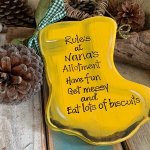 K&ouml;nnte beinhalten: Ein gelbes Holzschild in Form eines Stiefels mit dem Text "Rule's at Nana's Allotment Have fun Get messy and Eat lots of biscuits".