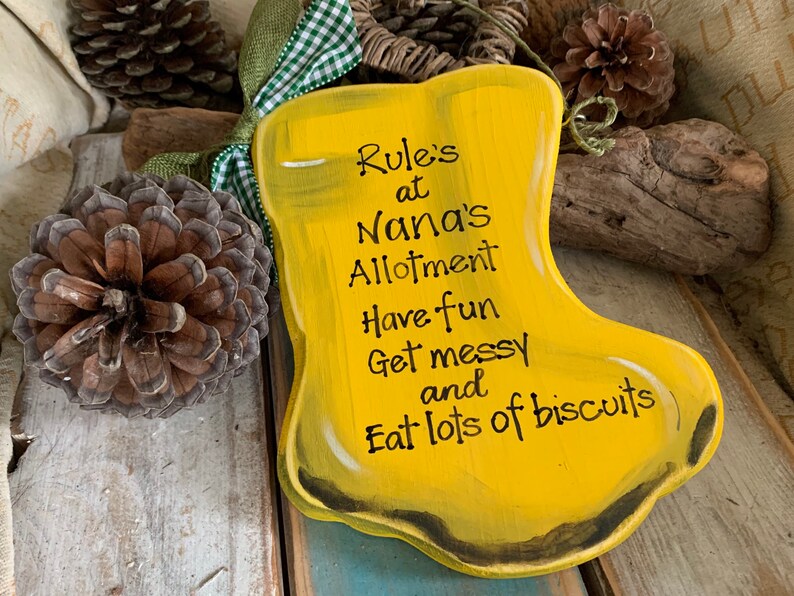 K&ouml;nnte beinhalten: Ein gelbes Holzschild in Form eines Stiefels mit dem Text "Rule's at Nana's Allotment Have fun Get messy and Eat lots of biscuits".