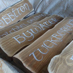 Pu&ograve; includere: Cinque cartelli in legno con lettere bianche. I cartelli recitano "Hobbiton", "Michel Delving", "Bywater", "Tuckborough" e "Bag End".