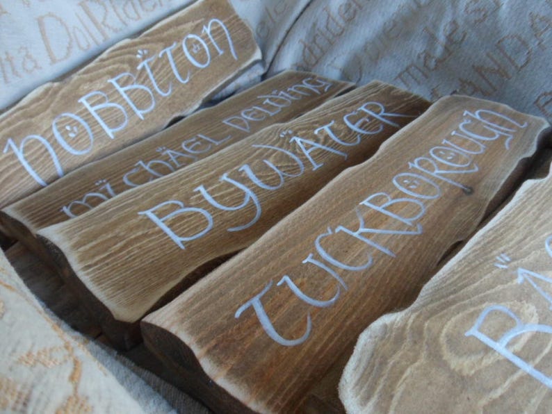 Pu&ograve; includere: Cinque cartelli in legno con lettere bianche. I cartelli recitano "Hobbiton", "Michel Delving", "Bywater", "Tuckborough" e "Bag End".
