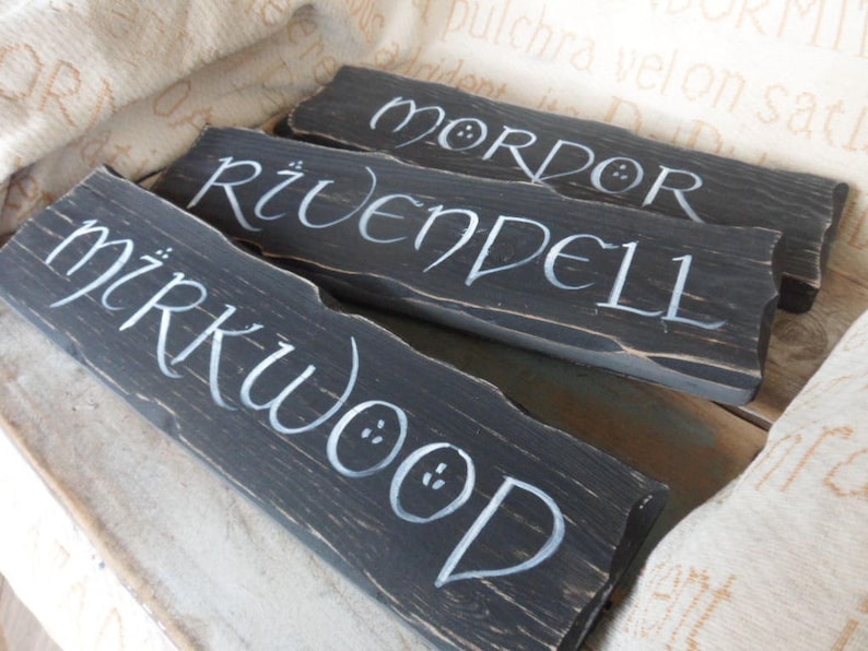 Pu&ograve; includere: Tre cartelli di legno dipinti di nero con lettere bianche. I cartelli recitano "Mirkwood", "Rivendell" e "Mordor".