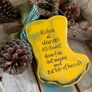 K&ouml;nnte beinhalten: Gelbes Holzschild in Form eines Stiefels mit dem Text "Rule's at Nana's Allotment Have fun Get messy and Eat lots of biscuits".