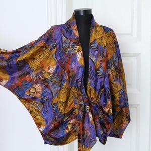 Puede incluir: Una chaqueta de manga larga y abertura frontal con un estampado abstracto colorido en tonos de morado, dorado y naranja. La chaqueta tiene un corte holgado y una silueta fluida.