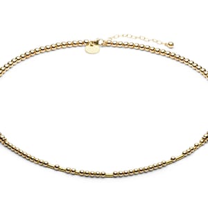 May include: A gold beaded necklace with a small gold clasp. The necklace is made of tiny, round beads and has a simple, minimalist design.