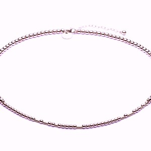 May include: A delicate rose gold necklace made of small beads with a simple clasp closure.