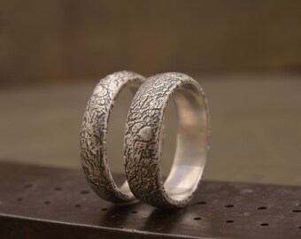 May include: Two silver wedding bands with a textured, hammered finish. The bands are stacked on top of each other.