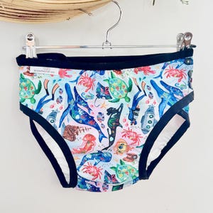 May include: Light blue underwear with a colorful sea life pattern, including whales, turtles, and jellyfish. The underwear has a black trim and a white interior. The text "branches of me" is visible on the waistband.