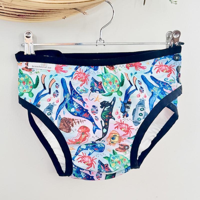 May include: Light blue underwear with a colorful sea life pattern, including whales, turtles, and jellyfish. The underwear has a black trim and a white interior. The text "branches of me" is visible on the waistband.