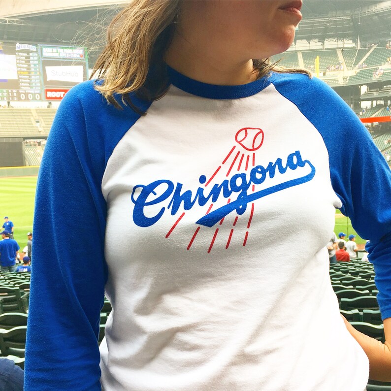 K&ouml;nnte beinhalten: Ein wei&szlig;es und blaues Baseball-T-Shirt mit einer blauen und roten Grafik, auf der "Chingona" steht, mit einer Baseball-Grafik &uuml;ber dem Wort.