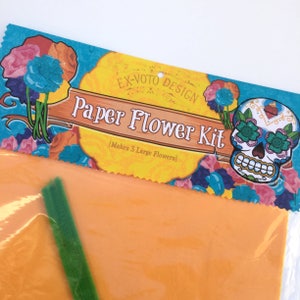 K&ouml;nnte beinhalten: Ein Papierblumen-Set mit einem farbenfrohen Design, das einen Zucker Sch&auml;del und Blumen zeigt. Das Set enth&auml;lt orange Seidenpapier und gr&uuml;ne Pfeifenreiniger. Die Verpackung lautet "Ex-Voto Design Paper Flower Kit (Makes 3 Large Flowers)"