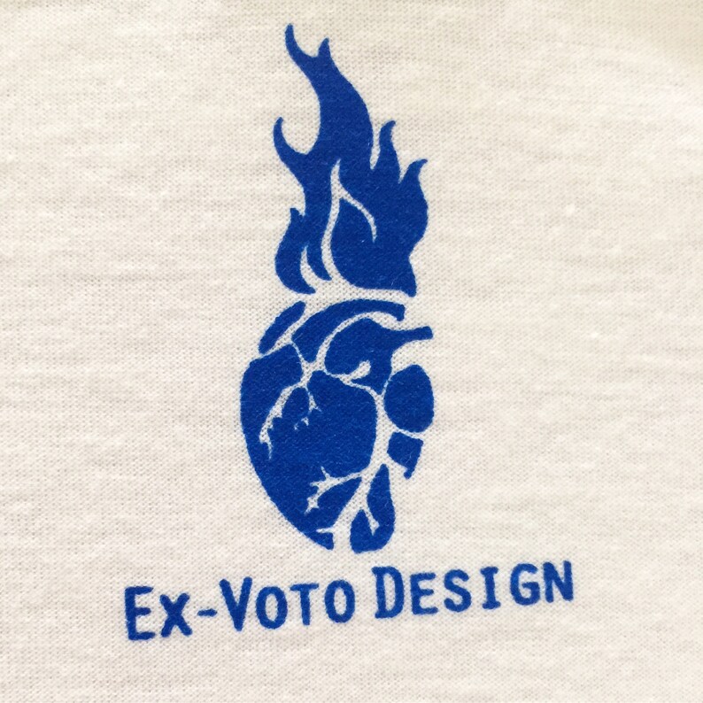 K&ouml;nnte beinhalten: Blaues Grafikdesign-Logo mit einem stilisierten Herz- und Flammenmotiv. Der Text "EX-VOTO DESIGN" befindet sich unterhalb der Grafik.