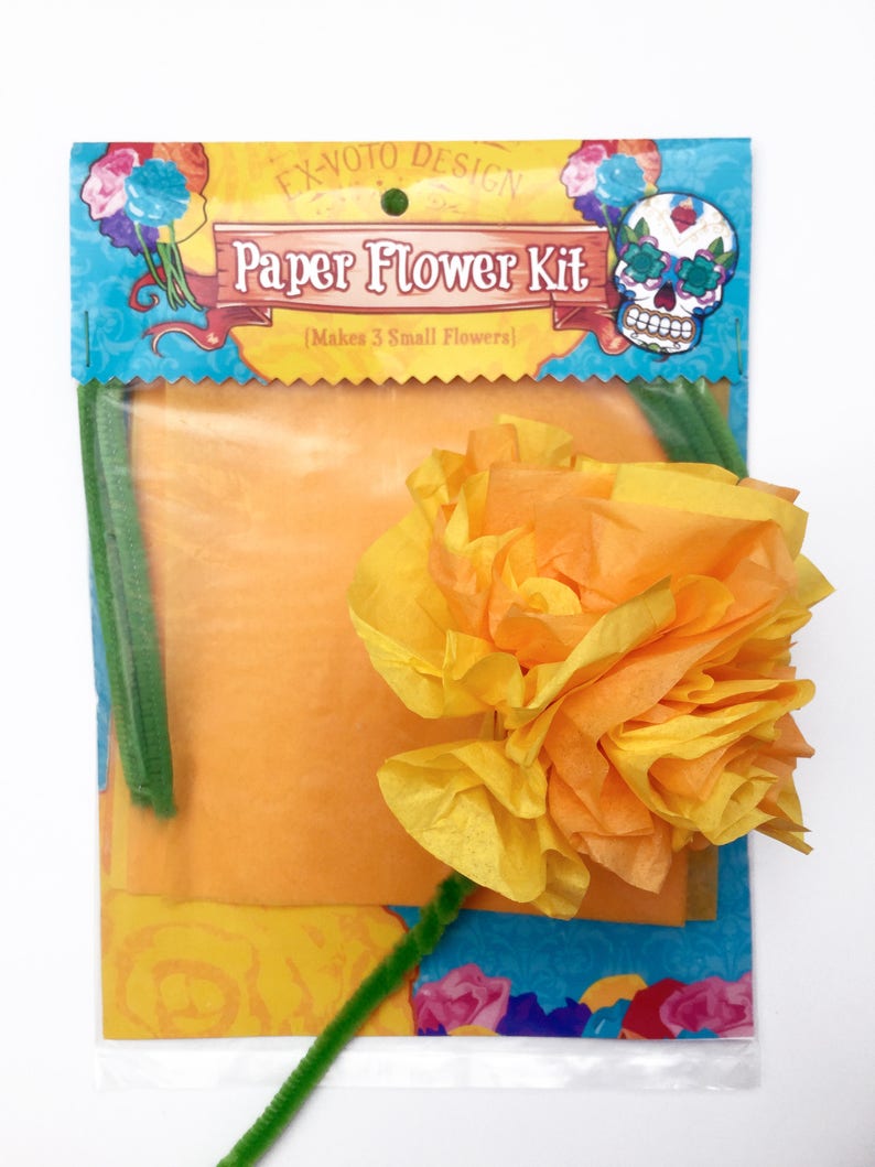 K&ouml;nnte beinhalten: Eine transparente Plastikt&uuml;te mit einem Papierblumen-Bastelset. Das Set enth&auml;lt drei gelbe und orangefarbene Seidenpapierblumen, drei gr&uuml;ne Pfeifenreiniger und Anleitungen. Die T&uuml;te hat ein farbenfrohes Design mit dem Text "Ex-Voto Design Paper Flower Kit [Makes 3 Small Flowers]" und einer Totenkopfgrafik.