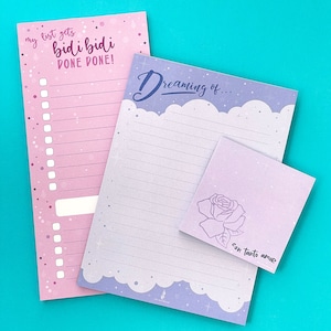 May include: A collection of stationery items, including a pink list notepad with the text "my list gets bidi bidi DONE DONE!", a lined notepad with the text "Dreaming of...", and a small square notepad with a rose illustration and the text "con tanto amor".