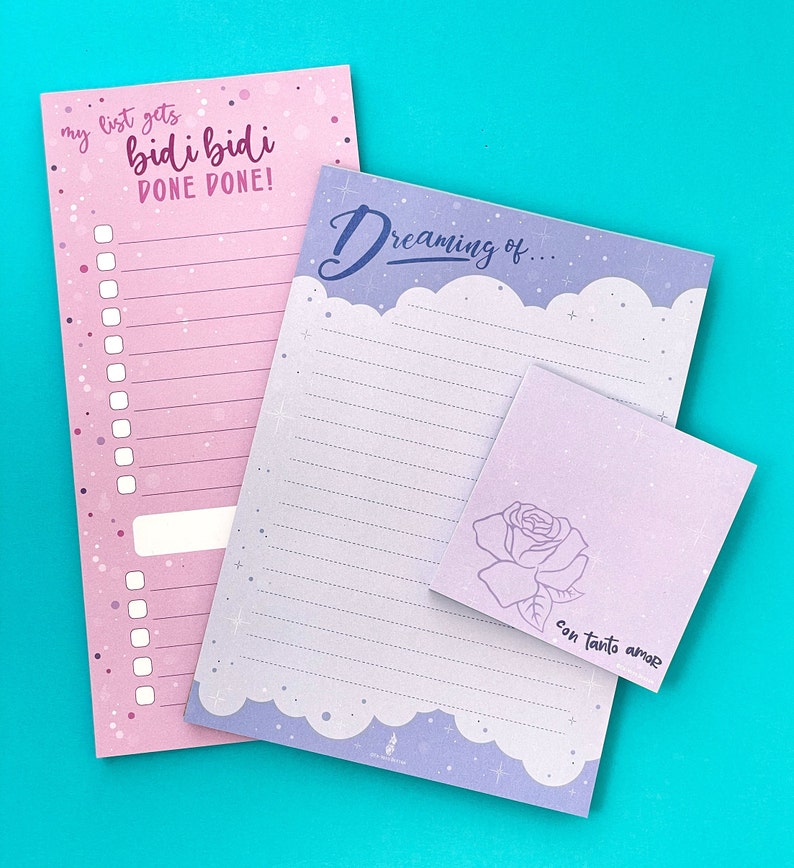 May include: A collection of stationery items, including a pink list notepad with the text "my list gets bidi bidi DONE DONE!", a lined notepad with the text "Dreaming of...", and a small square notepad with a rose illustration and the text "con tanto amor".