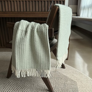 Peut inclure: Deux jetés en tissu gaufré vert avec des franges blanches drapé sur une chaise en bois.
