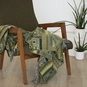 May include: A green armchair with a patterned throw blanket draped over it. The chair has wooden arms and legs. A potted plant is visible in the background.