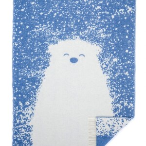 Puede incluir: Una manta tejida azul y blanca con un diseño de oso polar. La manta tiene un borde de flecos.