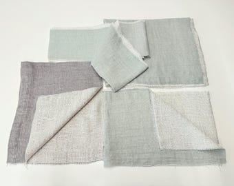 May include: A collection of rectangular fabric pieces in shades of sage green and muted gray. Each piece features a visible woven texture and raw, frayed edges. The fabric is layered, showing both the smooth top surface and the textured underside.