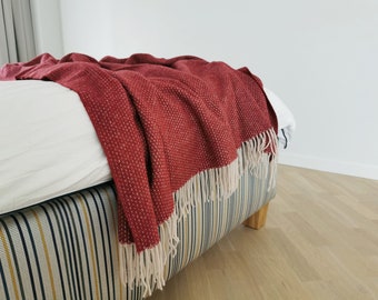 May include: A red throw blanket with a white fringe, draped over a bed with a striped headboard.