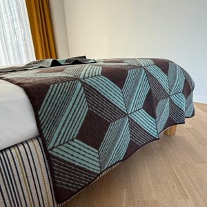 May include: A woven throw blanket featuring a geometric pattern of dark brown and light blue stripes. The design consists of repeating diamond and star shapes created by alternating colored lines across the entire surface of the textile.