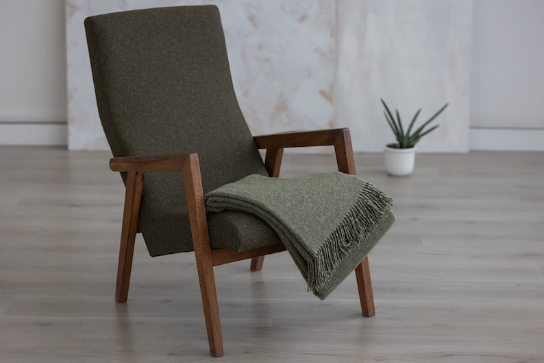 Puede incluir: Un sill&oacute;n verde con brazos y patas de madera, una manta de lana verde est&aacute; colocada sobre el sill&oacute;n.