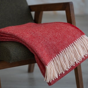 May include: A red herringbone throw blanket with white fringe draped over a wooden armchair.