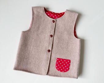 May include: A sleeveless vest featuring a light beige herringbone pattern on the exterior and a red lining with white polka dots. The front includes three dark brown buttons for closure and a single patch pocket with a red and white polka dot pattern.